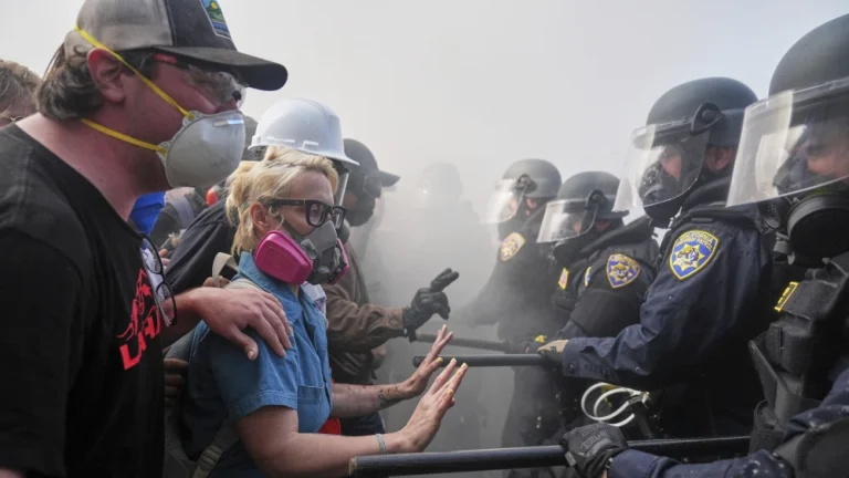 Protesters in respirator masks confront riot-gear police during an ICE immigration raid in Los Angeles, moments before false “Soros bricks” claims flooded social media.