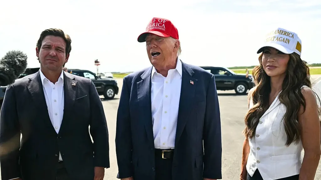 Donald Trump with Ron DeSantis and Kristi Noem at Florida detention center, wearing MAGA hats, standing in front of vehicles during Alligator Alcatraz tour